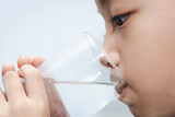 Fototapeta Łazienka - little Asian boy drinks water from a glass. shot of a child drinking a glass of cold water.