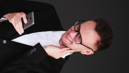 Vertical video. Romantic chat. Online flirt. Happy cheerful business man in love texting message on phone sending air kiss isolated on black.