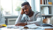 © Marta B - A man appears fatigued as he rests his head in his hand while studying at a desk with open books, suggesting exhaustion or frustration during a study session.
