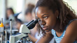 © Marta B - A student closely examines a specimen through a microscope in a science class, displaying a focused and serious demeanor while engaged in learning.