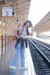 © Wuttichaik - Rear view of a young woman with backpack standing on a train station, travel concept, Portrait of Asian woman tourist waiting for the train at railway station