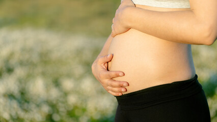 Woman pregnancy. Motherhood concept. Pregnant woman hugging belly in closeup. Defocused nature background and space for copy