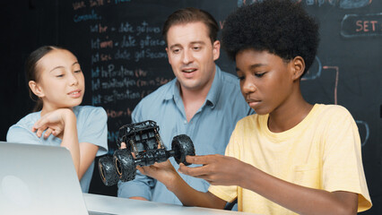 Wall Mural - Smart teacher inspect car model construction to diverse student. Highschool children with mixed races listening mentor explain robotic model system at table with laptop and wires placed. Edification.