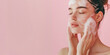 © julijadmi - Beautiful woman model washes her face with foam against pink background with copy space.