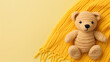 A small knitted amigurumi bear toy on a yellow blanket, on a yellow background. Flat lay, top view, copy space. space for text