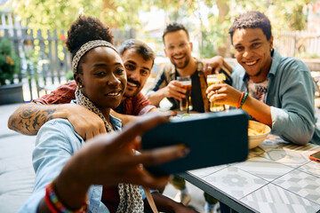 Wall Mural - Happy black woman taking selfie with her friends in cafe.