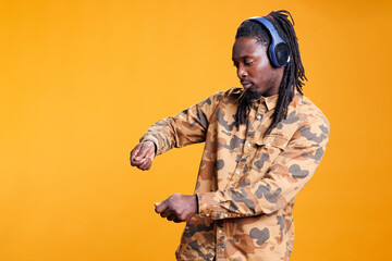 Wall Mural - African american man dancing and vibing on favourite music in studio over yellow background, enjoying free time. Joyful adult wearing headset, having fun with dance while showing funny moves