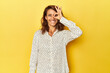 Middle-aged woman on a yellow backdrop excited keeping ok gesture on eye.