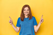 Redhead in blue t-shirt on yellow backdrop indicates with both fore fingers up showing a blank space.