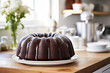 Chocolate bundt cake topped with chocolate glaze on white table in light and bright kitchen