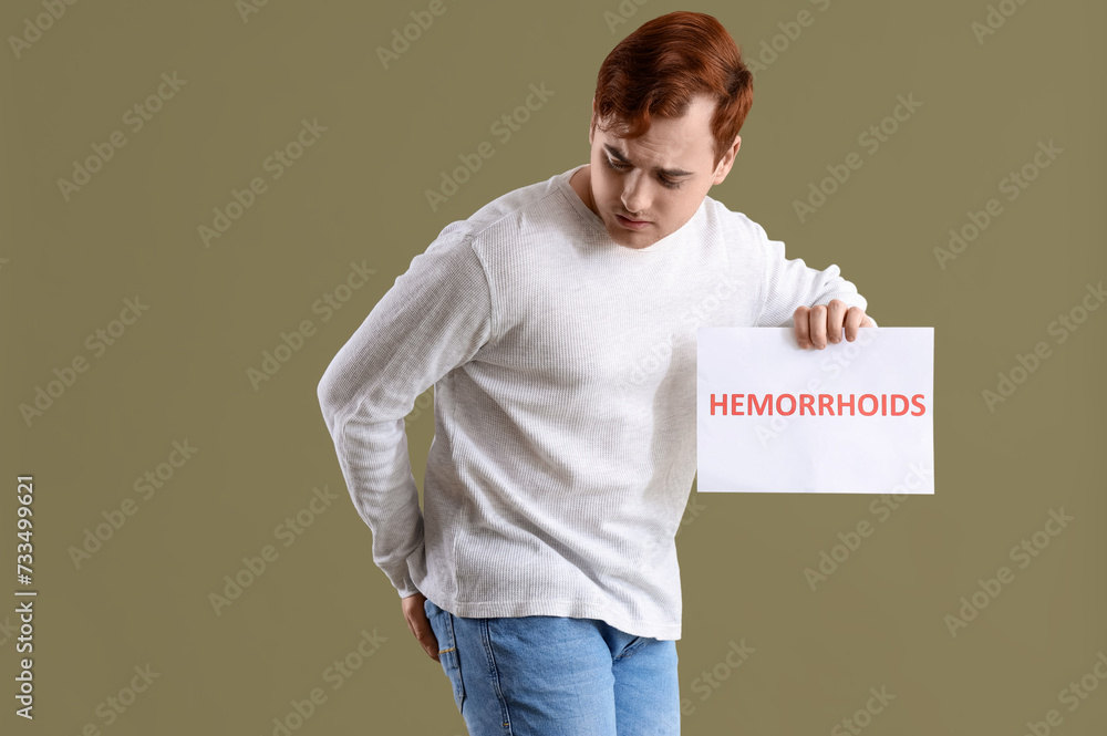 Young man holding paper with word HEMORRHOIDS on green background