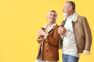 Sticker - Mature couple in sheepskin coats with coffee cups on yellow background