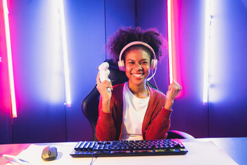 Wall Mural - African American girl gaming streamer team winner playing online fighting with Esport wearing headphones in neon lighting room. Talking other players planing strategies to win competitors. Tastemaker.