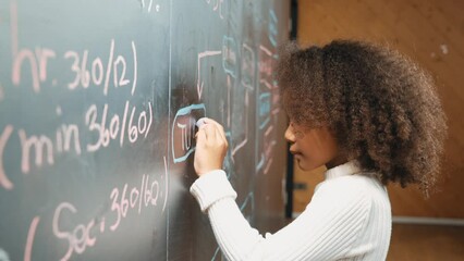 Site view of young african girl writing engineering prompt or code on blackboard. Skilled smart student planing a project by using coding and programing system in STEM technology classroom. Erudition.