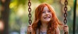 Red haired girl with freckles gleefully swinging at a playground, portraying happiness and joy.