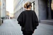 Back of a young white woman in a blank black sweatshirt outdoors.