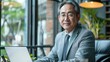 © mariiaplo - Senior Asian Businessman Using Laptop in Modern Cafe Setting