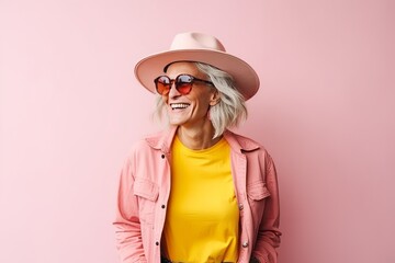 Wall Mural - Portrait of a happy senior woman in hat and sunglasses over pink background