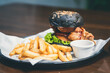 Close-up of a charcoal burger bun filled with fried chicken with french fries as a side dish. Chicken burger in the restaurant.