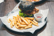 Close-up of a charcoal burger bun filled with fried chicken with french fries as a side dish. Chicken burger in the restaurant.