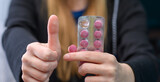 Fototapeta  - Kobieta trzyma w dłoni różowe tabletki i trzyma kciuk podniesiony w górę 