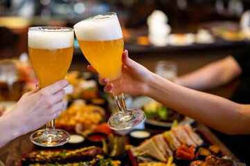 Wall Mural - Two friends woman hands clinking glasses of craft beer at the pub or bar