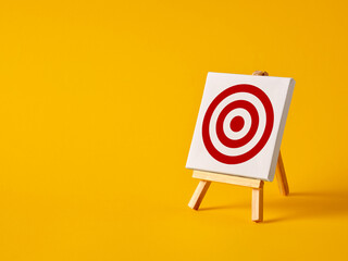 Wall Mural - a canvas with target goal symbol on an easel with yellow background with copy space.