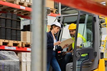 Wall Mural - Forklift driver talking with manager in modern industrial factory. Warehouseman reading order, order picking. Warehouse worker preparing products for shipmennt, delivery, checking stock in warehouse.