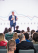 Blurred male speaker with presentation, in front of attentive audience in a conference or seminar setting.