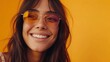 © Z A C - Smiling woman with long brown hair and large round orange-tinted sunglasses against a vibrant yellow background.
