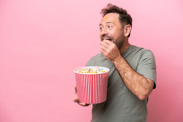 Wall Mural - Middle age caucasian man isolated on pink background holding a big bucket of popcorns