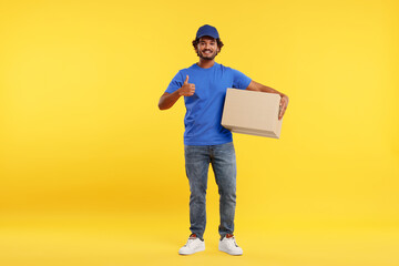 Canvas Print - Happy young courier with parcel showing thumb up on orange background