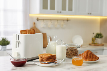 Making toasts for breakfast. Appliance, crunchy bread, honey, jam, milk and croissant on white marble table in kitchen