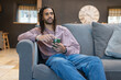 © Cultura Creative - Man with dreads relaxing on sofa and using phone