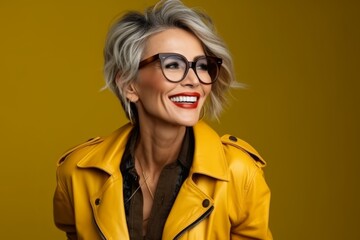 Wall Mural - Portrait of young happy smiling woman in yellow jacket and glasses, over yellow background