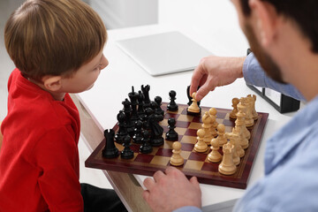 Wall Mural - Father and son playing chess at table indoors, closeup