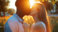 A Young Interracial Couple Shares A Tender Kiss Against The Golden Hues Of Sunset, Framed By The Soft Glow And Serene Park Ambiance