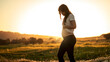 Pregnant woman park. Woman posing in the park with the sunset and rays illuminating her pregnant belly. Woman showing her 3 month pregnant belly in the park