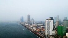 Aerial View Of Colombo, High-rises Along The Coast, Urban Landscape. Foggy Weather Masks Distant Buildings, Waves Lap On The Shore, City Life Buzz Below.