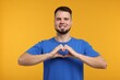 © New Africa - Man showing heart gesture with hands on golden background