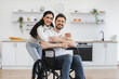 © sofiko14 - Portrait of young woman hugging Caucasian man with disability wearing casual outfit posing in spacious dining room. Positive young husband feeling optimistic while making recovery from injury at home.