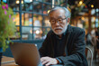 © Alexey - Elderly Asian man pondering while working on laptop in a coworking space. Reflective mood with copy space. Lifelong learning and productivity concept