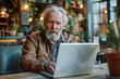 © Alexey - Elderly man with white beard focused on laptop in bright coworking area. Senior professional with copy space. Contemporary workspace and active retirement concept