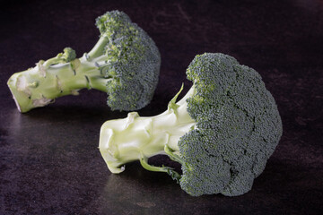 Two heads of fresh green broccoli on a solid black background. Isolated. Modern.