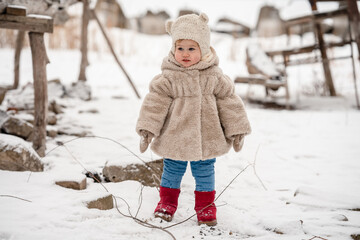 Wall Mural - Cute little baby child toddler in a plush hat and fur coat on a snowy winter landscape with reeds. A cozy winter season, an active childhood, the baby looks like a teddy bear