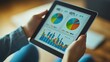 © Rattanathip - Hands holding a tablet displaying colorful pie charts and bar graphs, indicating active business data analysis.