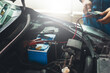 © chartphoto - Auto mechanic uses multimeter to check the voltage level in a car battery during a vehicle maintenance procedure..