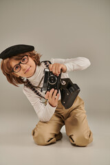 Wall Mural - young photographer in beret with retro camera sitting on floor, curious boy in suspenders