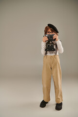 Wall Mural - young photographer in beret and suspenders holding retro camera while standing in studio