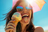 Fototapeta  - Cheerful, young woman eating colorful ice cream and sticking tongue out